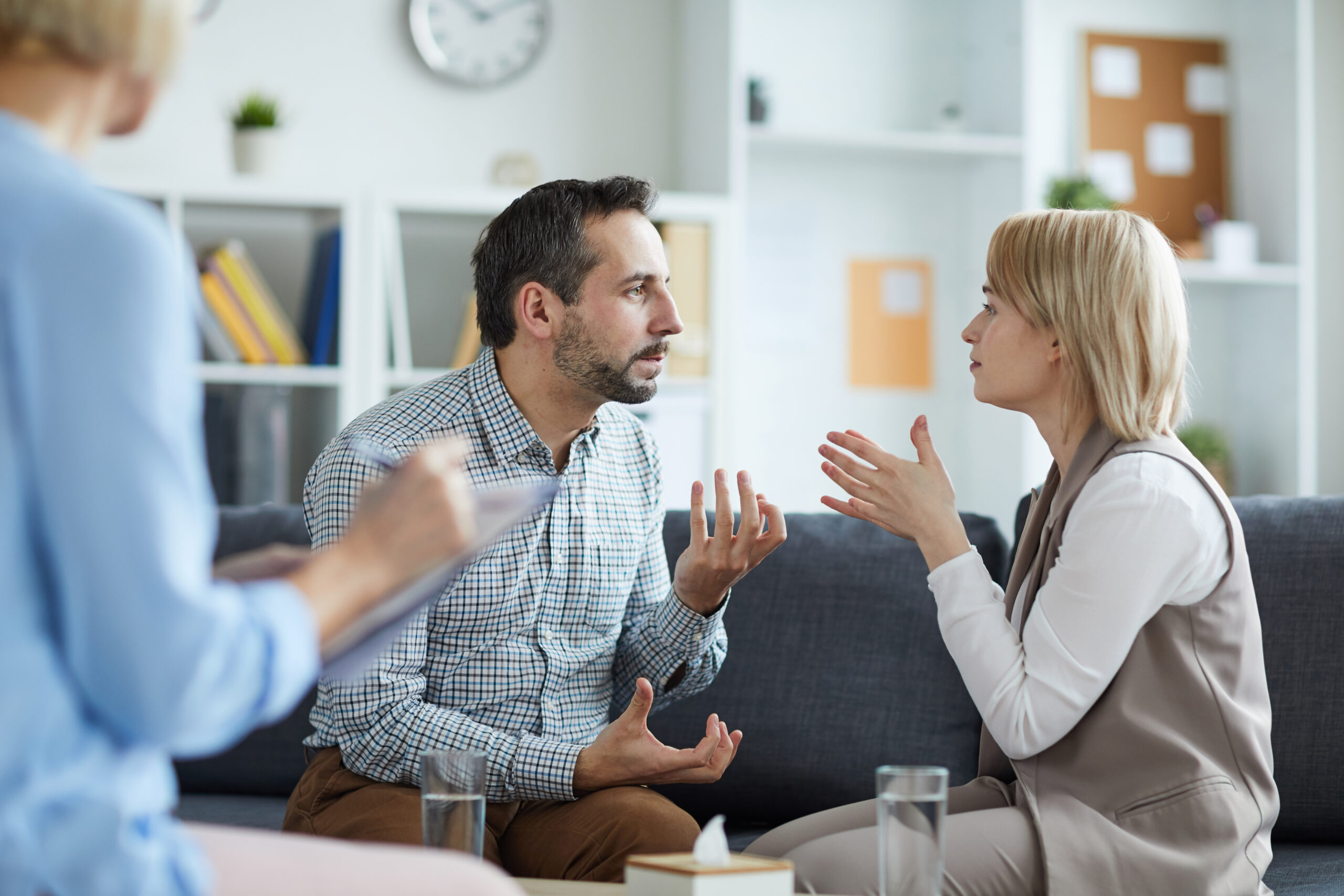 Young annoyed man and woman sitting on couch and blaming one another on their troubles while visiting family counselor