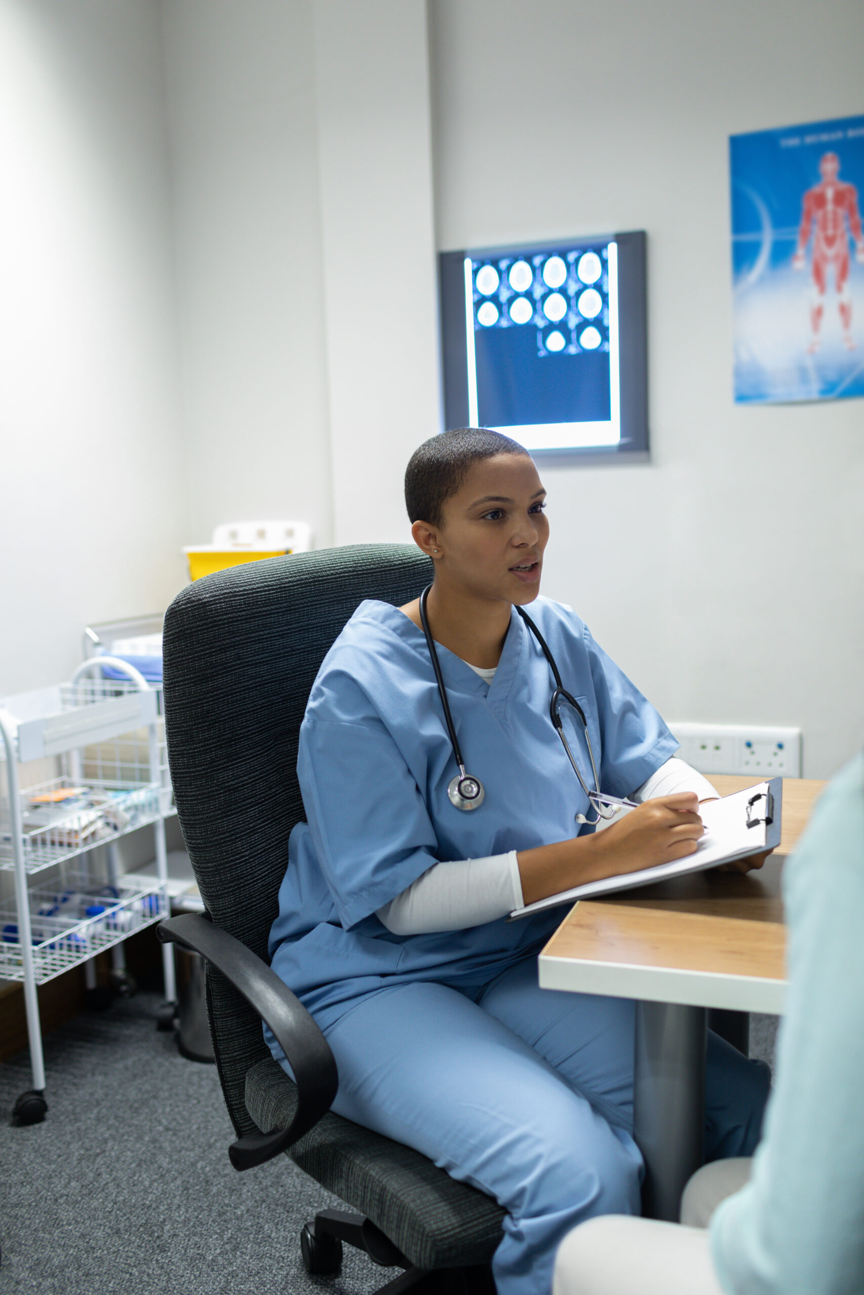 Front view of mixed-race female doctor giving prescription to woman at desk in hospital