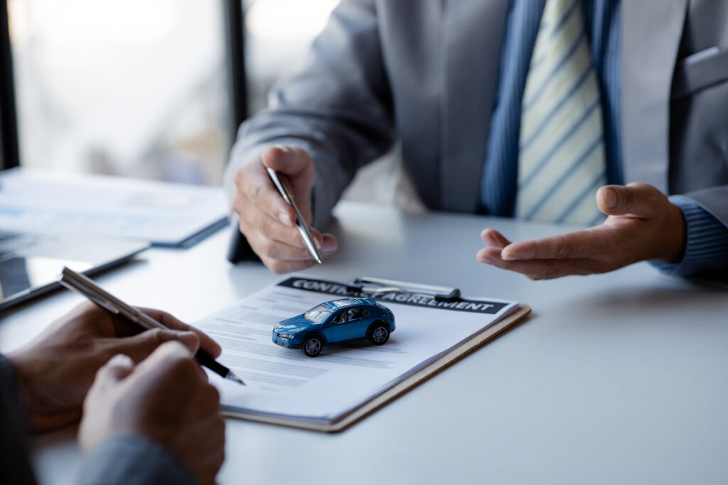 Clipboard with a blue car on table and people in formal business clothes sitting across the table