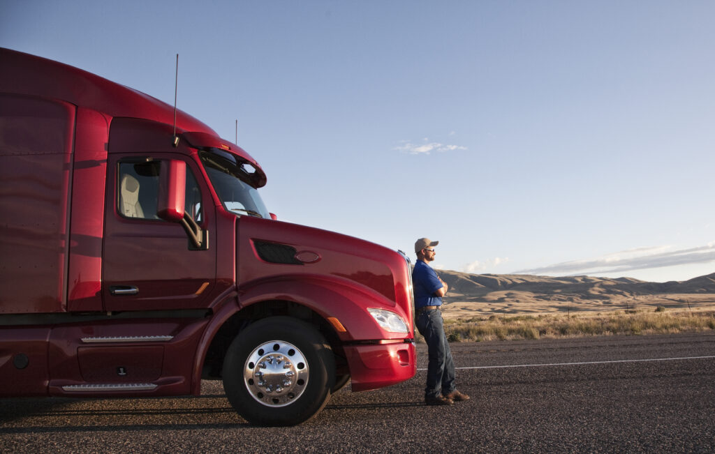Truck driver leaning on the grill of his commercial truck.